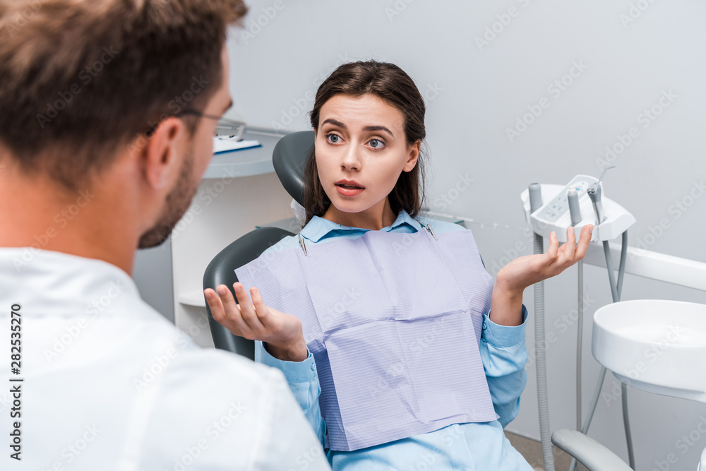 Obraz premium selective focus of attractive woman showing shrug gesture near dentist in clinic