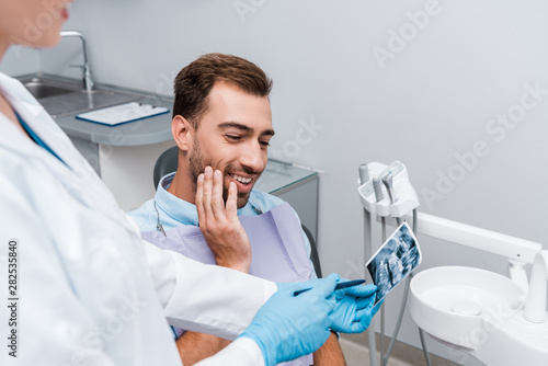 Canvas Print selective focus of cheerful man looking at x-ray near dentist in white coat