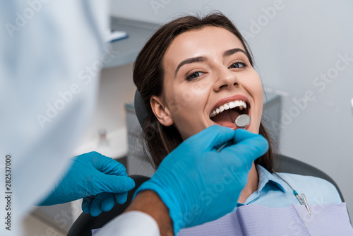 selective focus of dentist in latex gloves holding dental mirror near woman