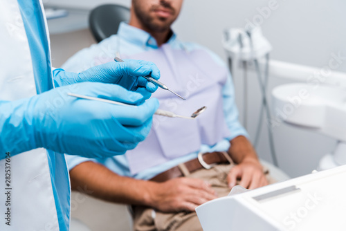 selective focus of dentist in blue latex gloves holding dental instruments near patient