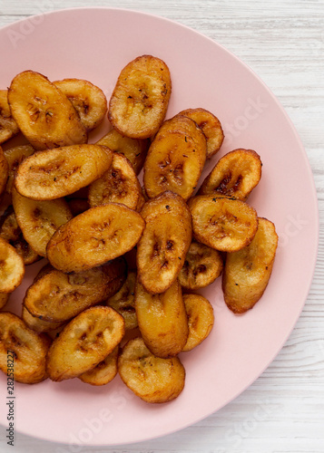Homemade fried plantains on a pink plate on a white wooden background, top view. Flat lay, overhead, from above.