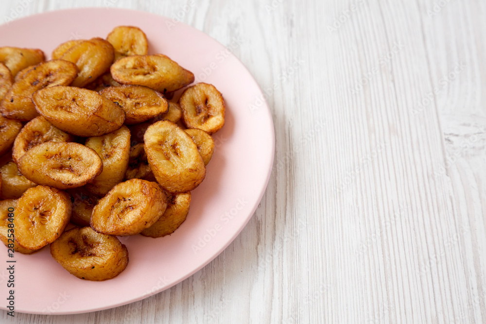 Homemade fried plantains on a pink plate on a white wooden background, low angle view. Copy space.
