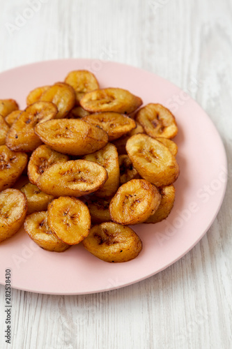 Homemade fried plantains on a pink plate on a white wooden surface, side view. Close-up. © Liudmyla