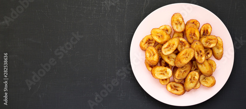 Slika na platnu Homemade fried plantains on a pink plate on a black surface, overhead view