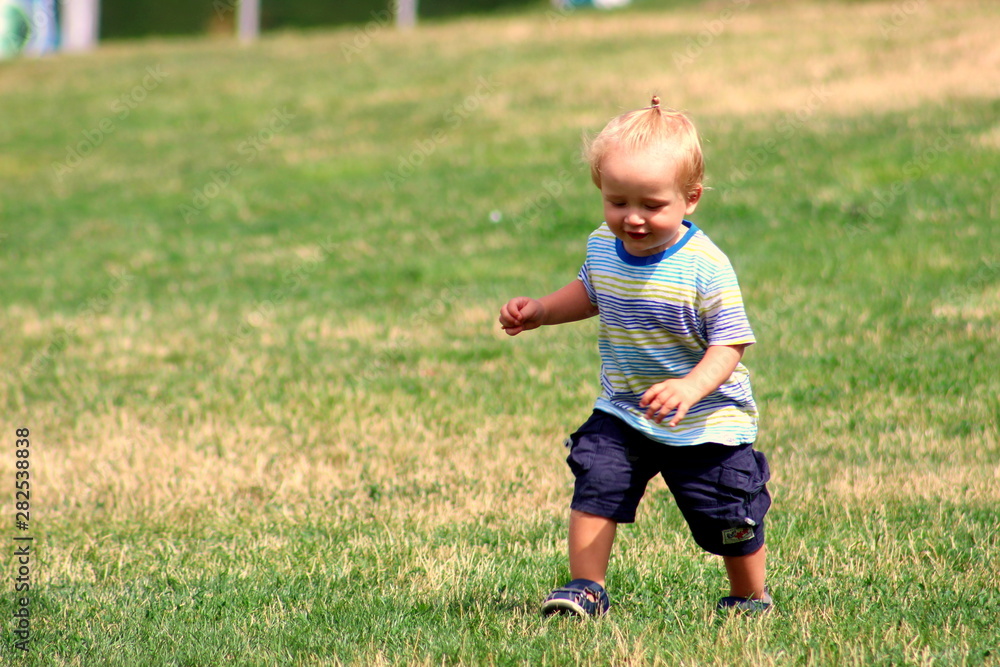 Cute toddler boy blond European appearance close-up in gray clothes in the park smiling selective focus. Cute toddler boy blond European appearance close-up in gray clothes in the park smiling selective focus.