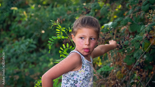 Authentic shot of a little girl with face smeared of berries is eating a fresh biologic blackberries just harvested by herself in a forest.