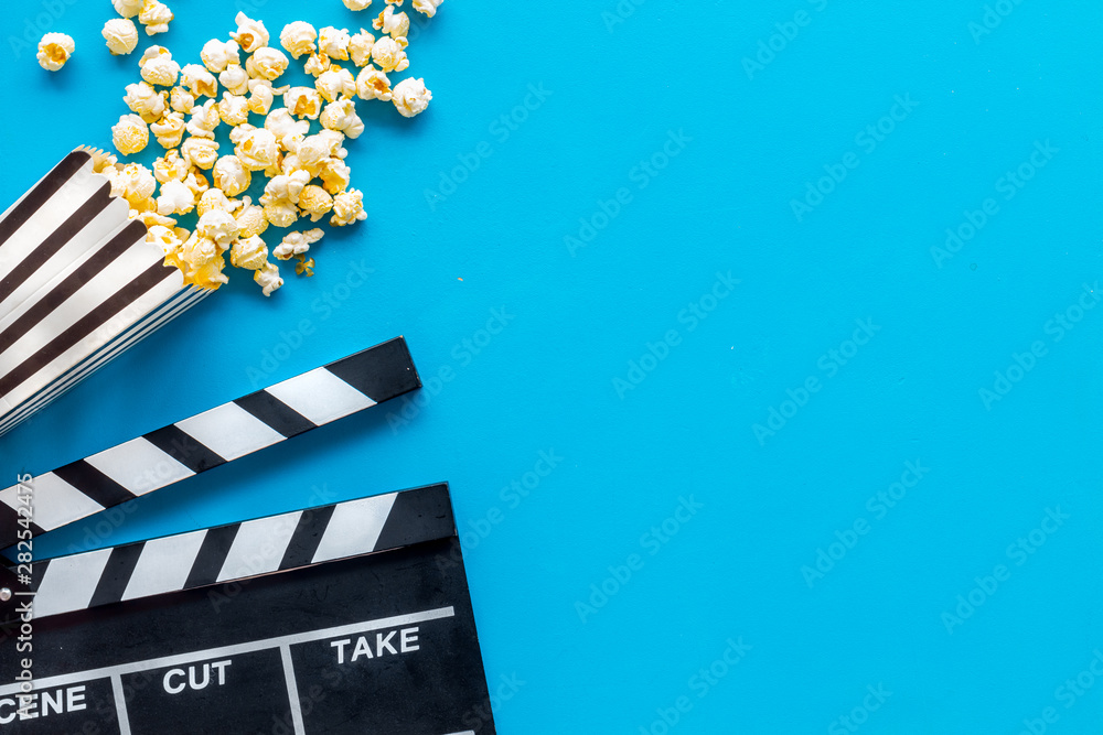 Movie premiere concept with clapperboard, popcorn on blue background top view space for text