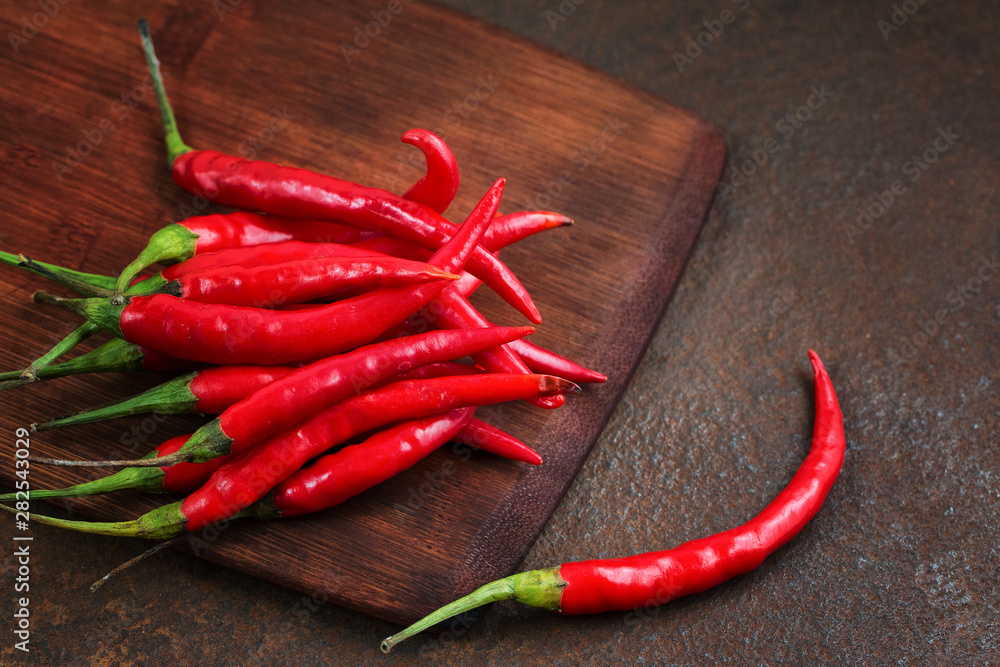 Pods of hot red pepper on a wooden board on a rusty metal surface. Pods of hot red pepper on a wooden board on a rusty metal surface.