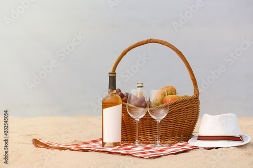 Wicker picnic basket with food and wine on blanket near sea