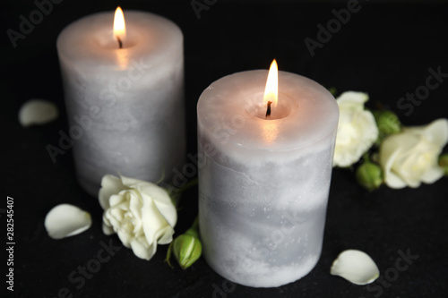 Burning candles and beautiful flowers on black table