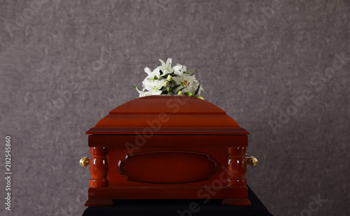 Wooden funeral casket with white lilies at grey wall photo