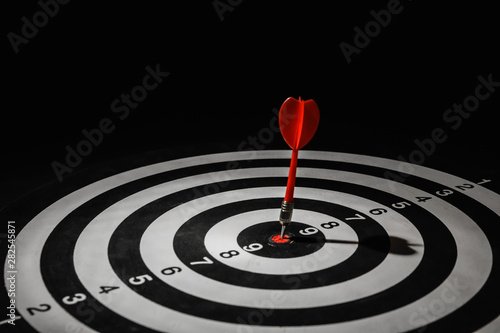 Red arrow hitting target on dart board against black background