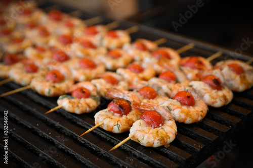 Delicious fresh shrimp skewers with cherry tomatoes on grill, closeup