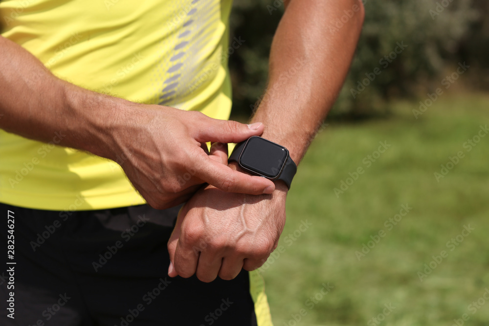 Young man checking pulse with smartwatch after training in park, closeup. Space for text