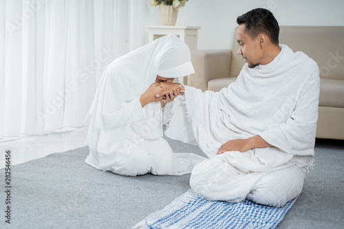 after sholat wife kissing husband's hand wearing white traditional clothes Ihram while sitting photo