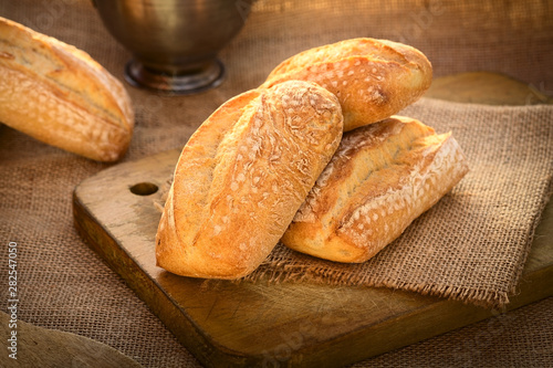 Fresh ciabatta buns on wooden board photographed with natural light (Selective Focus, Focus on the left bun on the board)