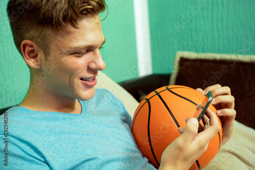 Beautiful teenager holding basketball ball and phone, closeup portrait indoors 