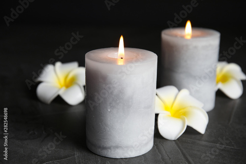 Burning candles and plumeria flowers on dark grey table