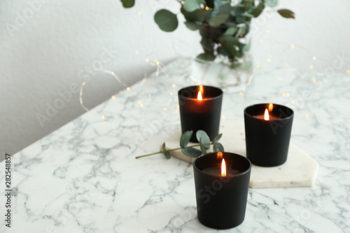Burning candles and green branches with fairy lights on marble table