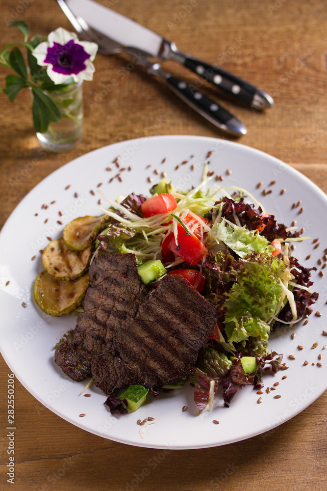 Beef salad: grilled beef steaks with tomatoes, cucumbers, zucchini, lettuce and cabbage, sprinkled with flax seeds. Home made food. Concept for a tasty and healthy meal Beef salad: grilled beef steaks with tomatoes, cucumbers, zucchini, lettuce and cabbage, sprinkled with flax seeds. Home made food. Concept for a tasty and healthy meal