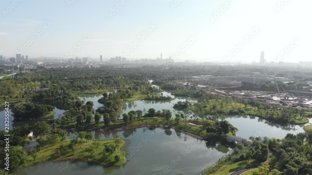 A drone flies over a large park, with walking paths and a large number of lakes. Guangzhou city is visible in the background A drone flies over a large park, with walking paths and a large number of lakes. Guangzhou city is visible in the background