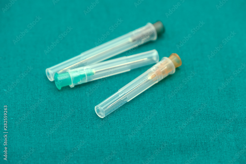 Obraz premium Three color of injection needle with cover isolated on surgical green drape