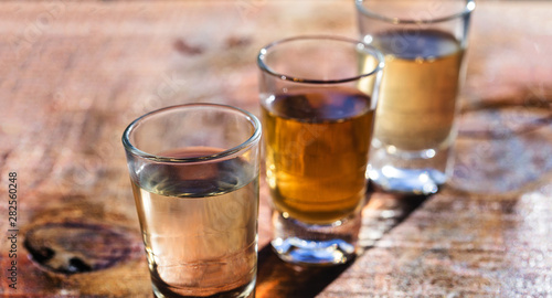 three shot glasses of Brazilian gold and white cachaca isolated on rustic wooden background. Typical drink from brazil.