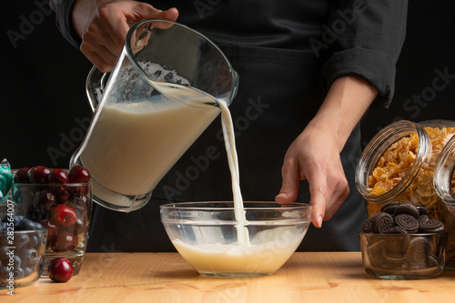 Pouring milk into the breakfast, freezing in motion. Cooking breakfast cereals, granules, breakfast cereals, cereals, berries of cherries, and blueberries, sweet cookies. On a black background photo