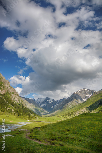 Idyllic summer landscape with hiking trail in the mountains with beautiful fresh green mountain pastures and snow-capped mountain tops in the background, National park. Nice view.