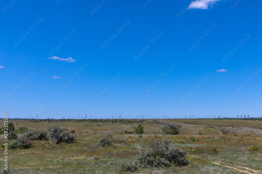 The russian steppe or prairie with ravines and blue sky near Volgograd city in the sunny summer day. The countryside landscape or view with electric lines or mains with grass, bushes and small trees 