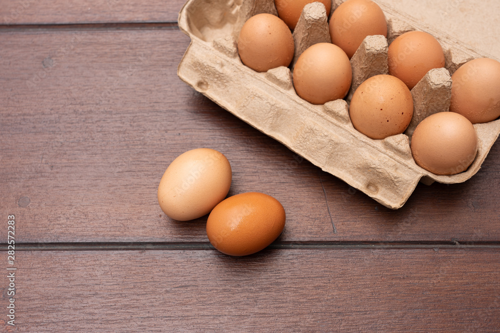 Close up of organic raw chicken eggs in egg box on brown wooden floor background Close up of organic raw chicken eggs in egg box on brown wooden floor background