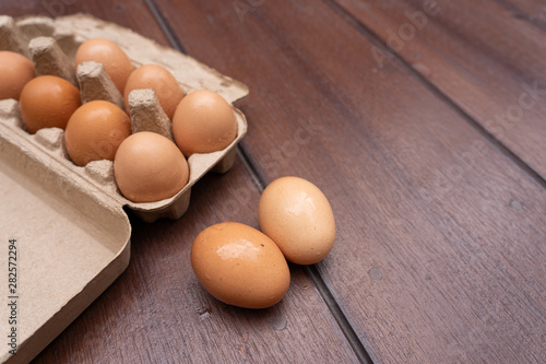 Close up of organic raw chicken eggs in egg box on brown wooden floor background