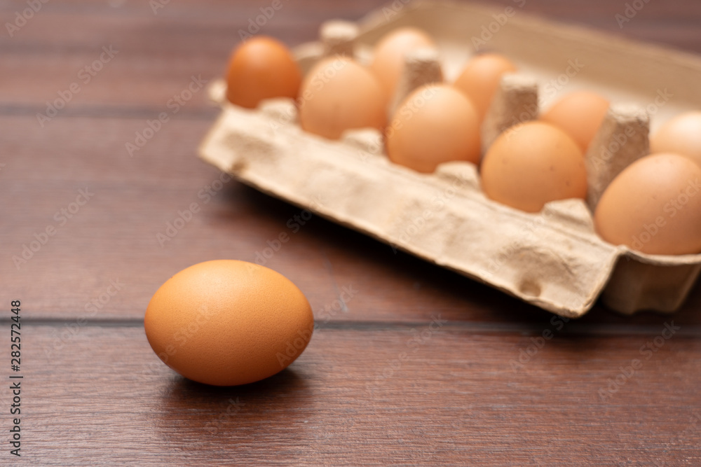 Close up of organic raw chicken eggs in egg box on brown wooden floor background Close up of organic raw chicken eggs in egg box on brown wooden floor background