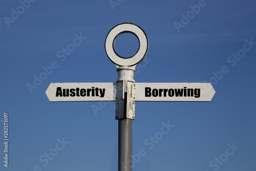 Old road sign with a choice between austerity and borrowing written on it.  Government fiscal policy concept