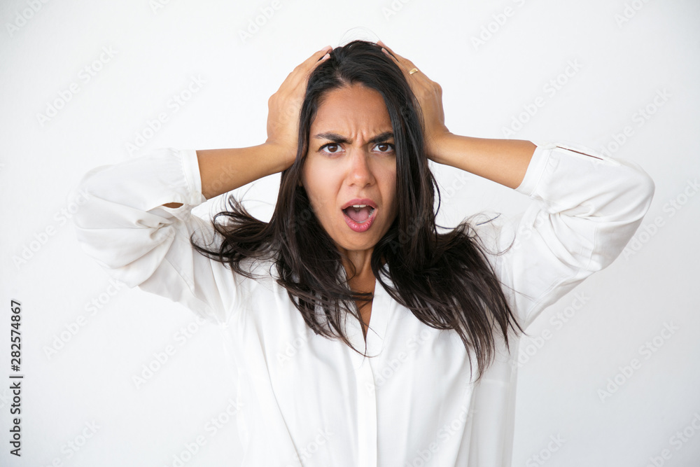 Stressed worried woman shocked with unexpected news. Frowning beautiful young Latin woman in white shirt holding head and gasping. Surprise or shock concept Stressed worried woman shocked with unexpected news. Frowning beautiful young Latin woman in white shirt holding head and gasping. Surprise or shock concept