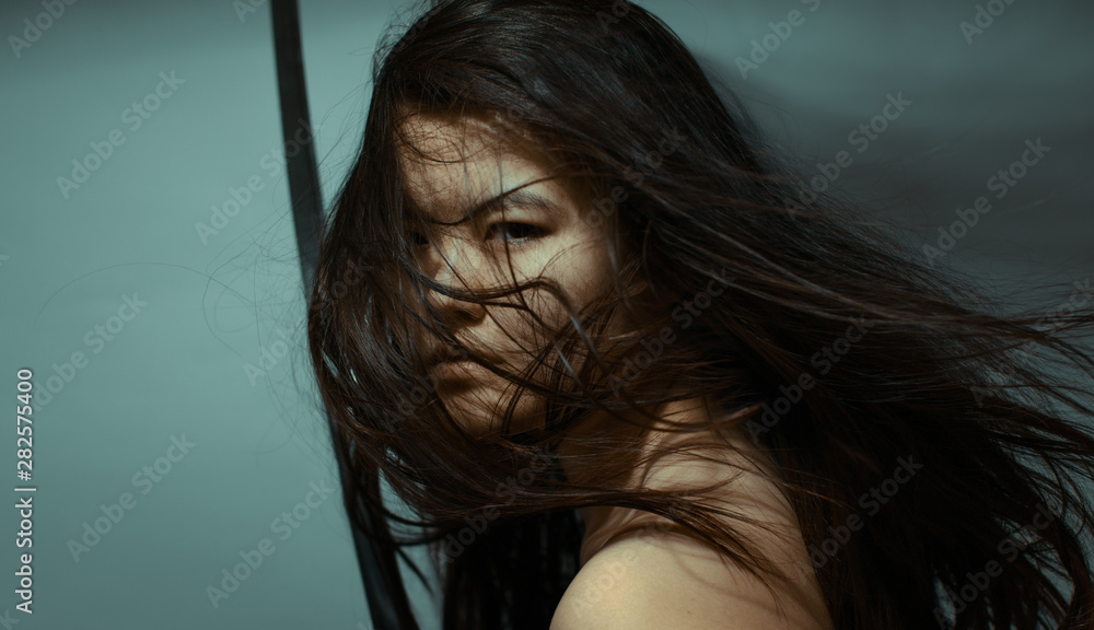 Oriental girl with streaming hair holding katana sword looking at you assasin sight with copyspace on background Oriental girl with streaming hair holding katana sword looking at you assasin sight with copyspace on background