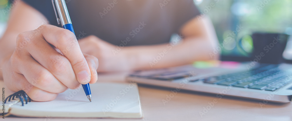 Woman hand is writing on a notepad with a pen in office.Web banner.