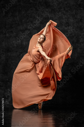 Ballerina. A young dancer dressed in a long peach dress, pointe shoes with ribbons. Performs a graceful, graceful dance movement. Beautiful classic ballet. Advertising ballet studio. Volumetric photos