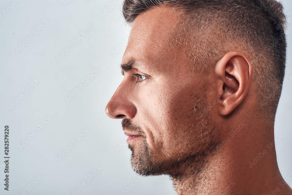 Everything is perfect. Side view of charming and confident man with a stubble standing against grey background Everything is perfect. Side view of charming and confident man with a stubble standing against grey background