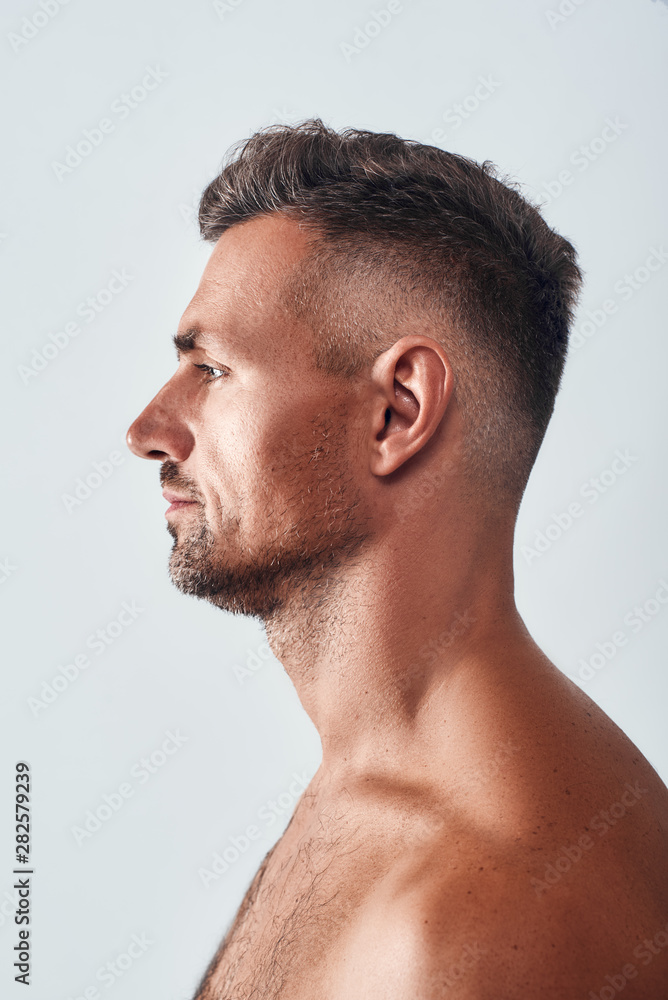 Confident and handsome. Side view of charming man with a stubble standing against grey background Confident and handsome. Side view of charming man with a stubble standing against grey background