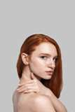 Confident in her beauty. Side view of young and beautiful redhead woman touching her neck while standing against grey background