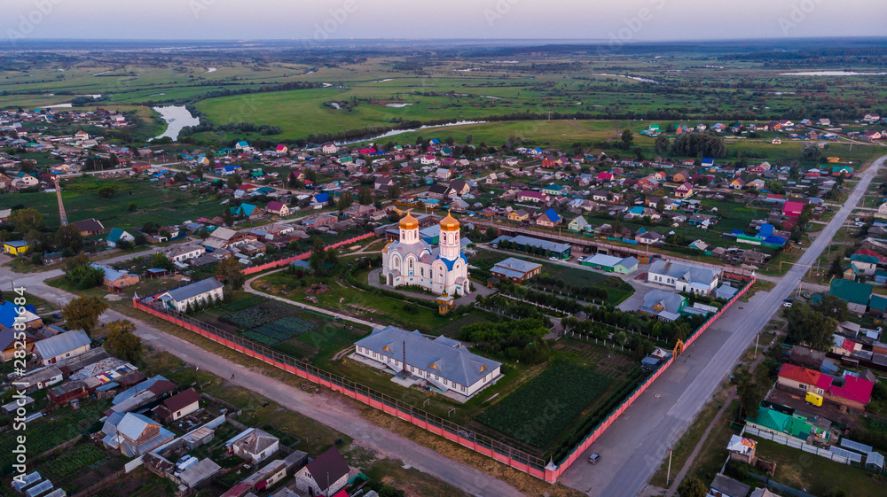 Aerial shot. Alexander Nevsky Temple in the center of the village, with many different houses around. Bright summer evening	