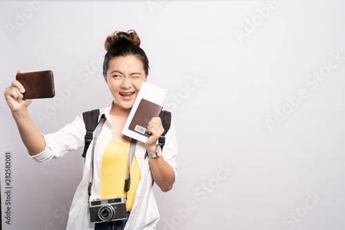 Woman taking selfie on smartphone and holding travel ticket isolated white background