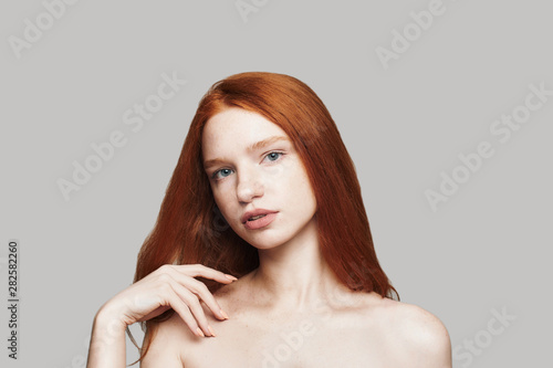 Feeling beautiful. Portrait of beautiful woman with long red hair looking at camera while standing against grey background