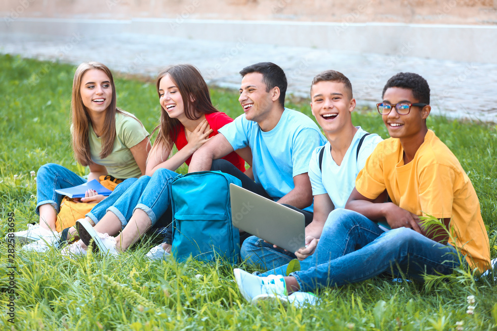 Obraz premium Portrait of young students with laptop sitting on grass outdoors