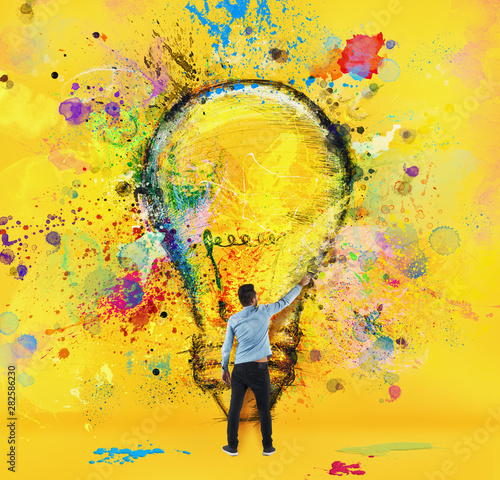 Boy draws with a brush a big light bulb. Concept of innovation and creativity. Yellow style photo