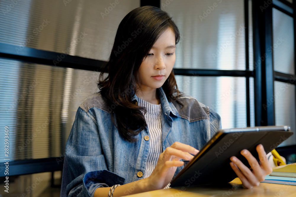 Young asian woman using digital tablet at home office background, casual office life, Asian female and digital tablet while working at home, People and technology concept Young asian woman using digital tablet at home office background, casual office life, Asian female and digital tablet while working at home, People and technology concept