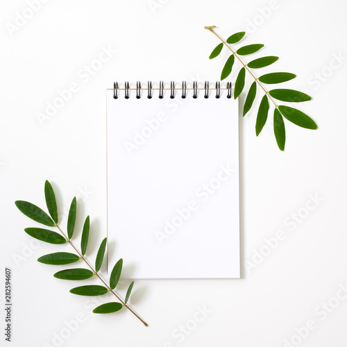 Marble paper blank, Notepad on white background. Flat lay, top view, copy space. Green leafs and blank notepad.