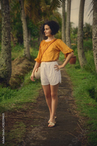 A girl in a white shorts on the path between the palm trees. Bali trip. Travel, adventure.