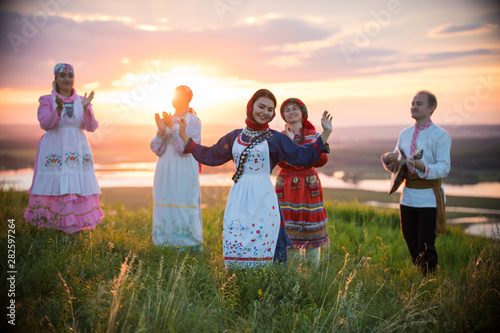 People in traditional russian clothes standing on the field on a background on the bright sunset - a woman dancing photo